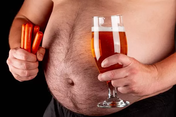 A man holds beer and smoked sausages against a large belly