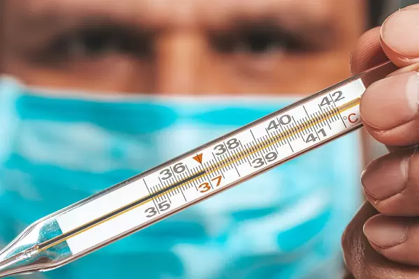 A man in a medical mask holding a thermometer
