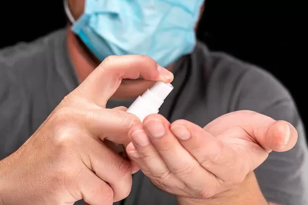 A man in a medical mask uses an antiseptic spray to disinfect his hands