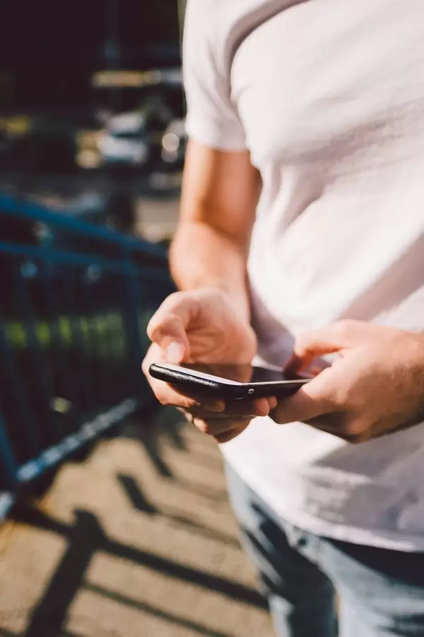 A man in a white T-Shirt uses his smartphone