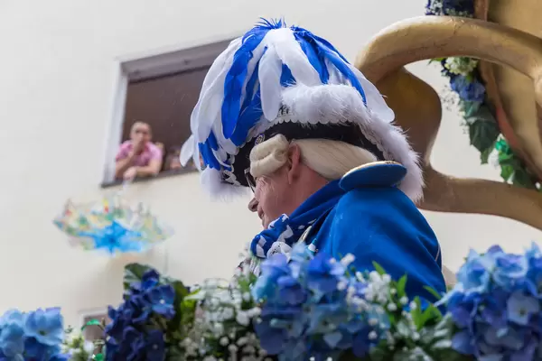 A man in traditional blue-white costume with wig and hat with blue-white feathers. He belongs to the traditional carnival society of the Blaue Funken in Cologne