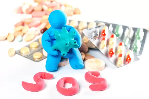 A man made of plasticine with a model of a virus in his hands and a lot of different pills, sign sos