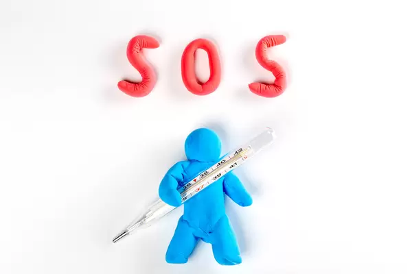 A man made of plasticine with a thermometer in his hands and the inscription SOS on white. Coronavirus concept