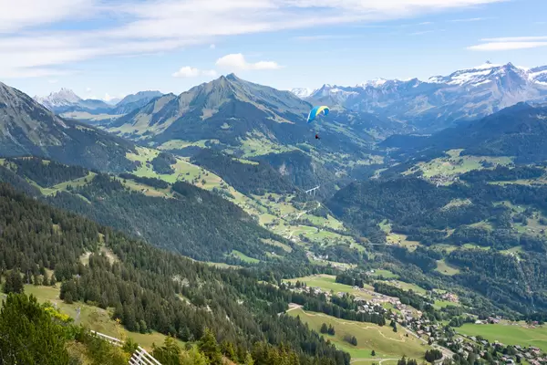 A man paragliding in Swiss mountains over a small town below