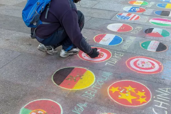 A man places coins on a country flag drawn with chalk on a market place