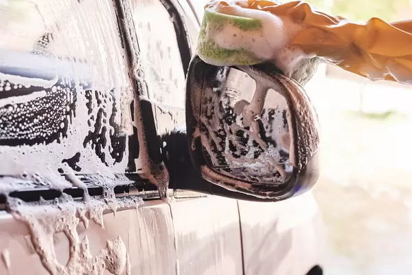A man washing the side-view mirror of an automobile