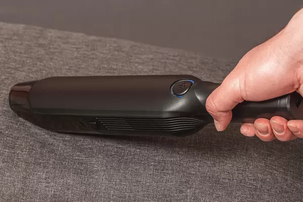 A man with a portable vacuum cleaner in his hand is cleaning the sofa