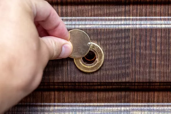 A man's hand opens the peephole on the door