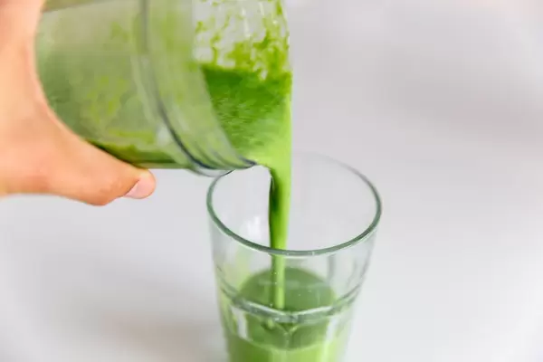 A man's hand pours a healthy green spinach-almond smoothie into a glass
