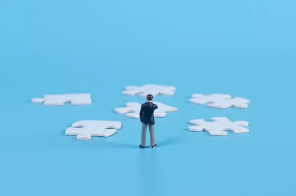A miniature businessman standing with a puzzle pieces