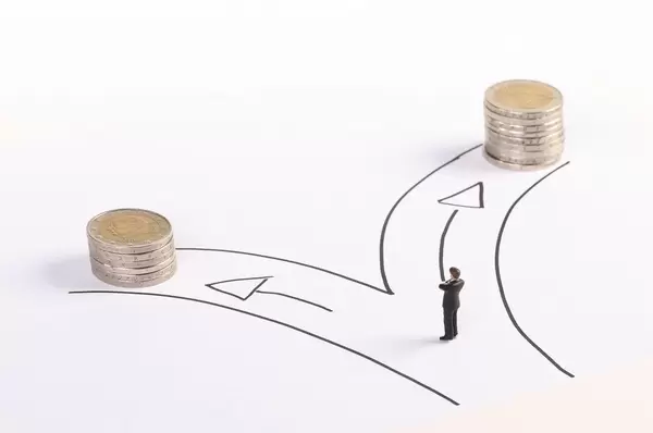 A miniature man standing in front of two paths with a stack of coins of different heights