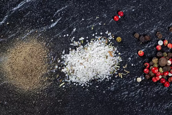 A mixture of peppers, ground black pepper and sea salt on a black background