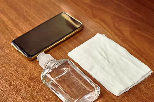 A mobile phone, disinfectant bottle and wipe on wooden table