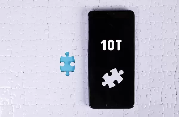 A modern big smartphone with a touch screen lies on a white jigsaw puzzle with 10T text