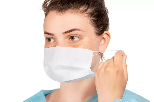 A nurse in a medical gown puts a disposable mask on her face