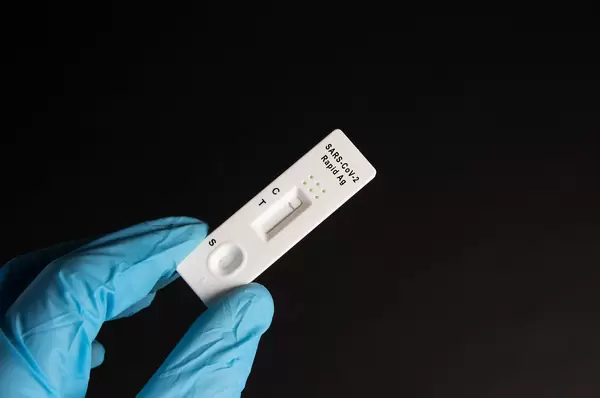 A nurse wearing latex gloves holds a covid-19 antigen test on black background