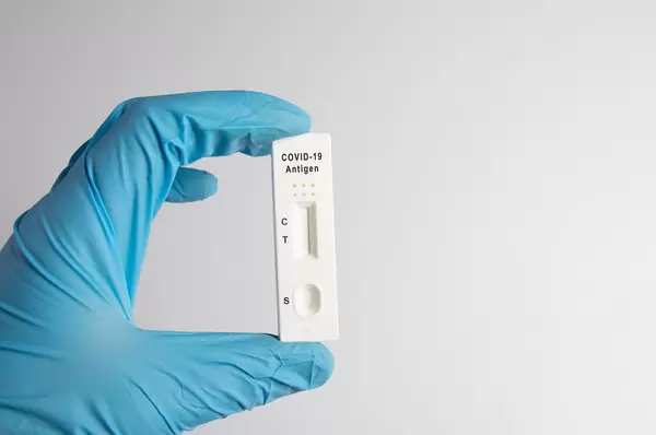 A nurse wearing latex gloves holds a covid-19 antigen test on white background