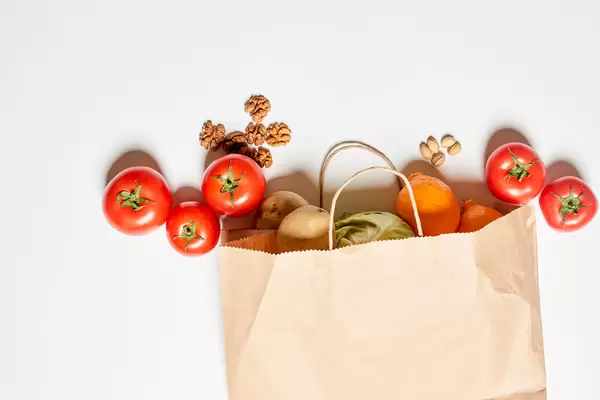 A paper shopping bag full of various organic vegetables and fruits on white background