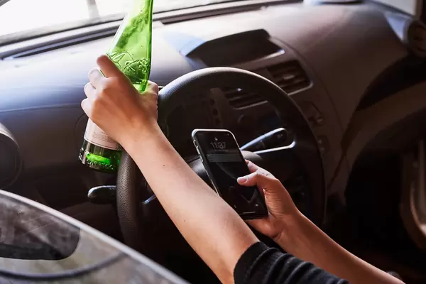 A person drinking beer and using a phone while driving a car
