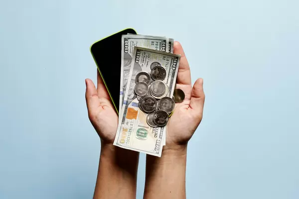 A person holding mobile phone and money