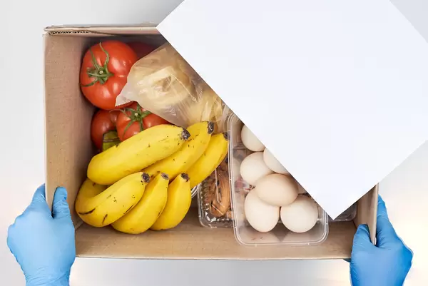A person in protective medical gloves holds a donation box with food items for a food pantry delivery