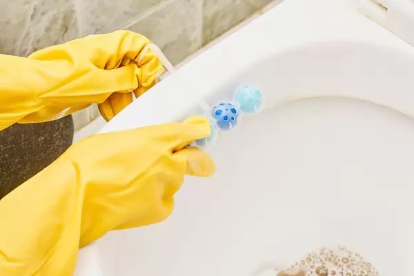 A person in rubber gloves hanging toilet rim refreshing block