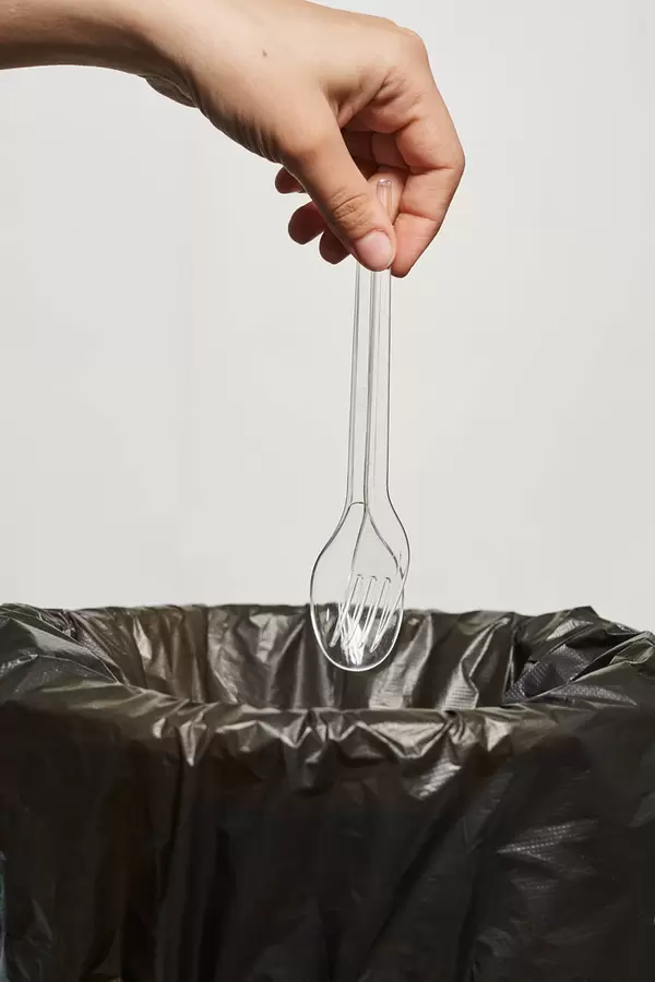 A person throws plastic fork and spoon into trash can