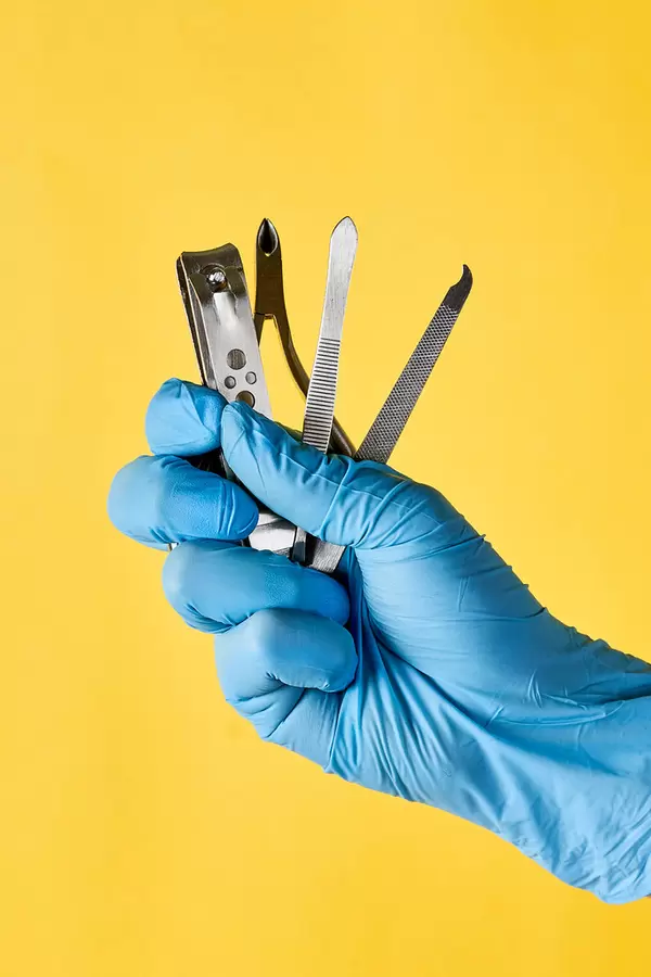 A person's hand in medical gloves holding manicure and pedicure tools