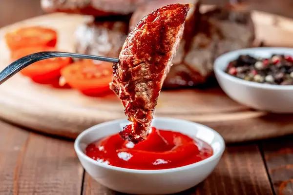 A piece of fried steak on a fork dipped in sauce