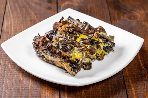 A piece of mushroom casserole with eggs and cheese in a white plate