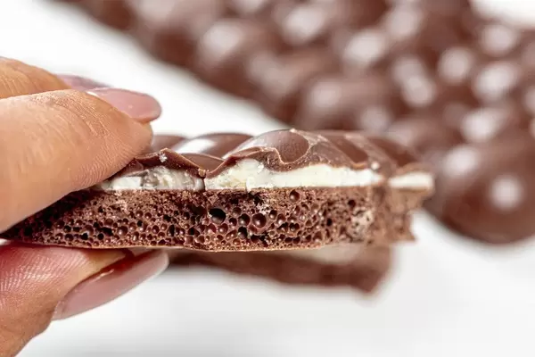 A piece of porous chocolate in a woman's hand closeup