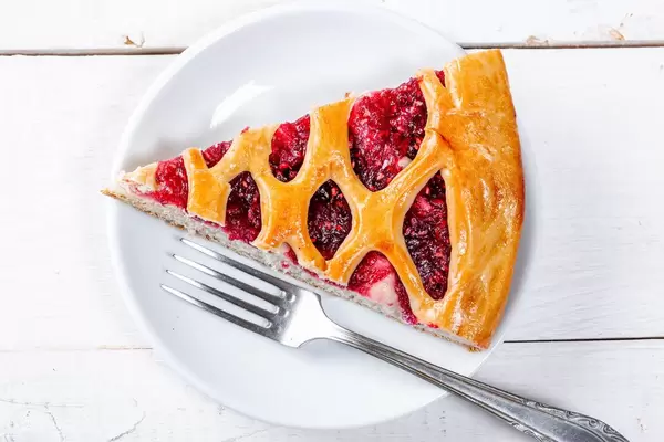 A piece of raspberry pie on a white plate with a fork. Top view