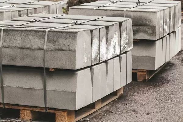 A pile of new road curbs outdoors on wooden pallets. Materials for road construction