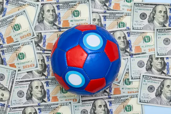 A pile of US dollar banknotes and a football ball on it