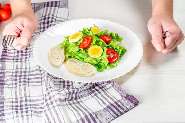 A plate of fresh salad and a man's hands with a knife and fork (Flip 2019)