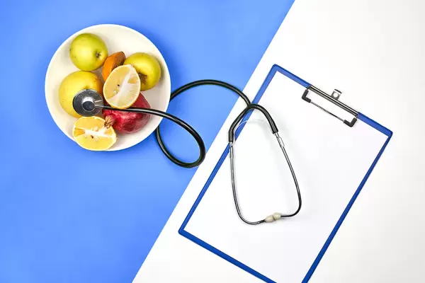 A plate of organic fruits, stethoscope and blank A4 paper on bright split-tone background