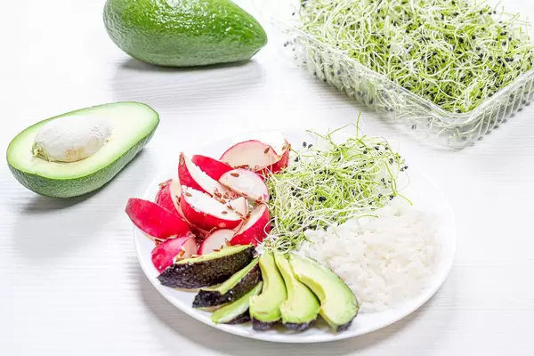 A plate of rice, radish, avocado and micro-greens onions on a white wooden background