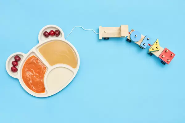 A plate of two types of baby purees and train toy on blue background