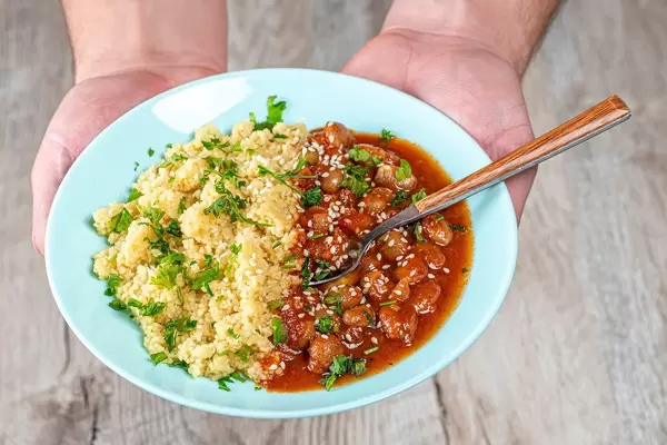 A plate of vegetarian lunch in the hands of a man. Beans in tomato sauce and couscous (Flip 2019)