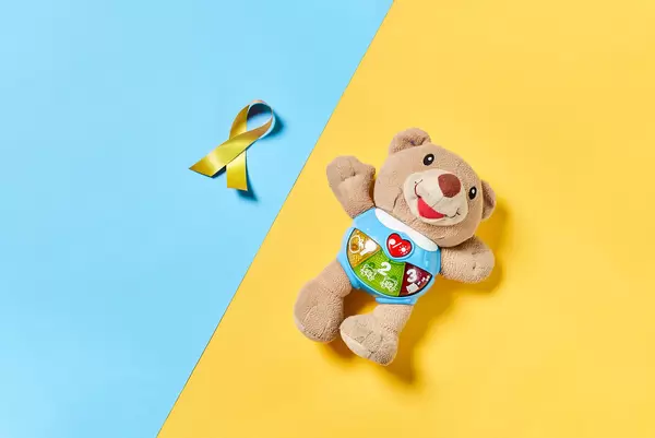 A plush bear toy and yellow gold ribbon, a symbol of childhood cancer awareness