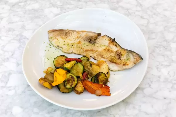A portion grilled swordfish with vegetables on a white plate