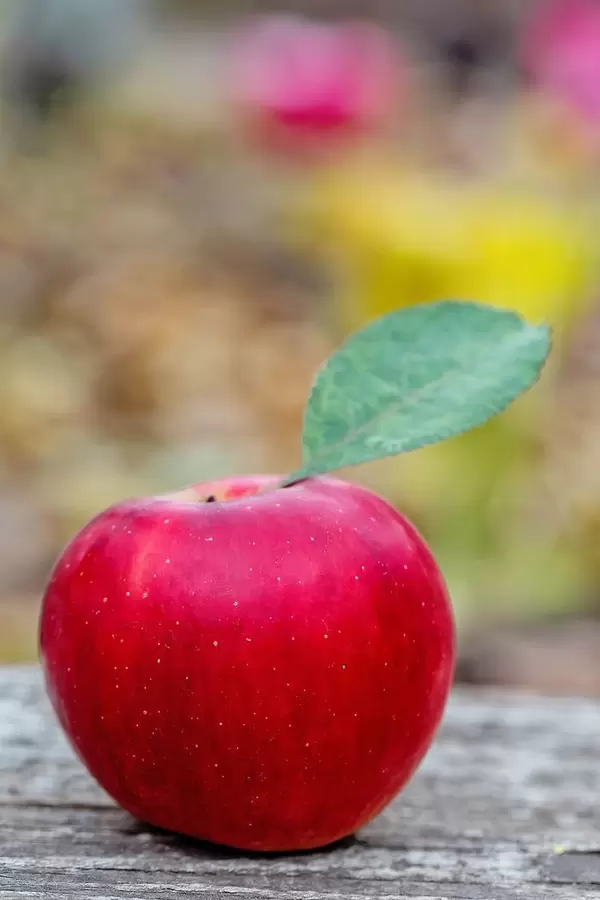 A red apple with the leave attched on a wooden table - close up