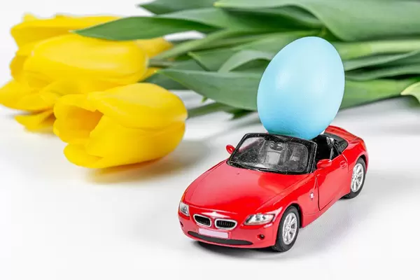 A-red-car-with-a-blue-Easter-egg-on-a-white-background-and-a-bouquet-of-yellow-tulips.jpg
