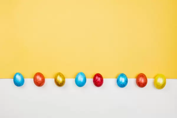 A row of colored Easter eggs on yellow and white background