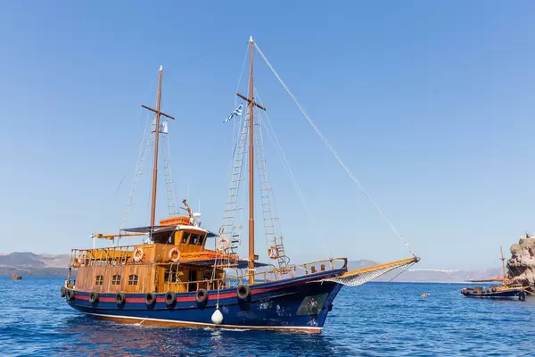 A sailboat with Greek flag by the coast in Santorini on a summer day