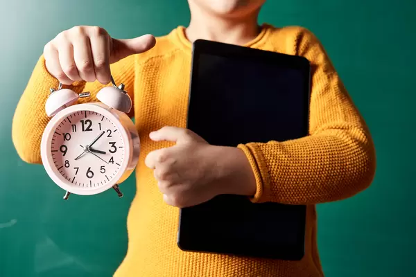 A schoolboy holds a tablet and alarm clock