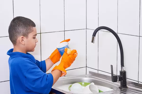 A schoolboy in blue shirt helping his mother with dishwashing