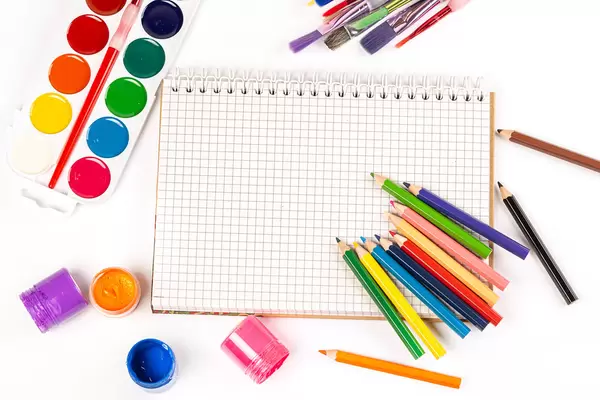 A set of paints, pencils, brushes for drawing and a notebook on white