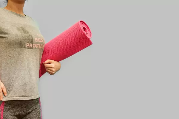 A slim lady with rolled yoga mat posing over grey background