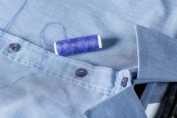 A spool of blue thread and needle on a man's shirt